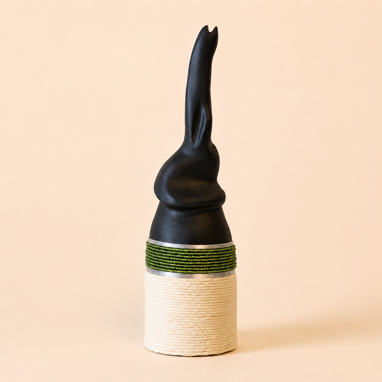 Black abstract carved elephant with a green beaded band on a beige background
