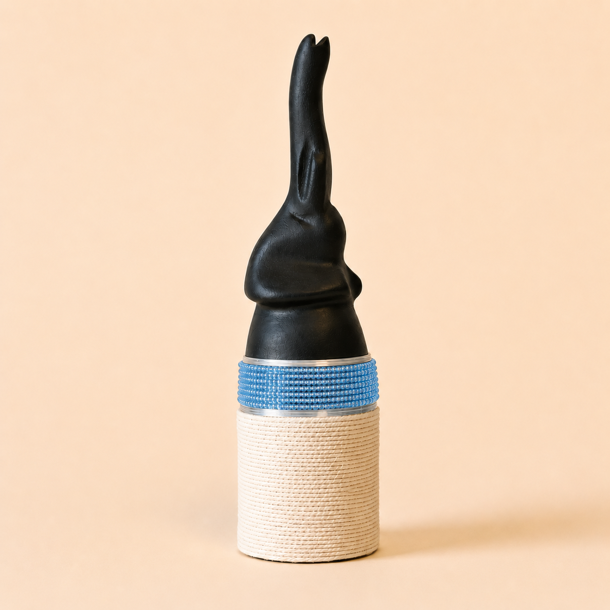 Black abstract elephant-shaped carving with a blue band and white base on a beige background