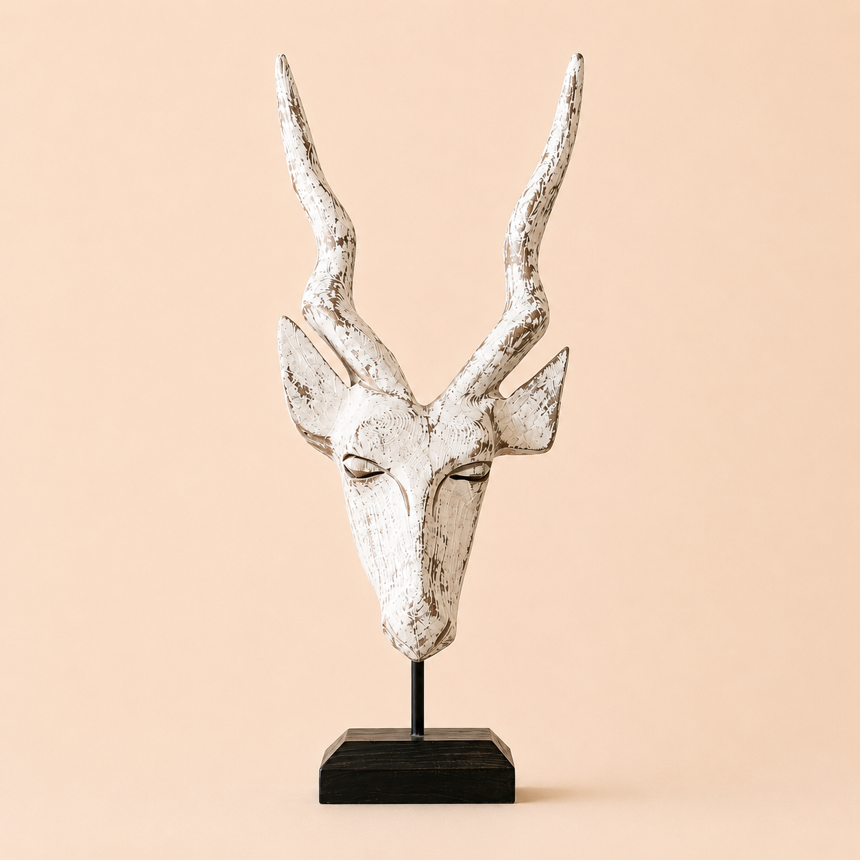 A wood carved antelope head on a stand with a white washed antique colouration on a beige background.