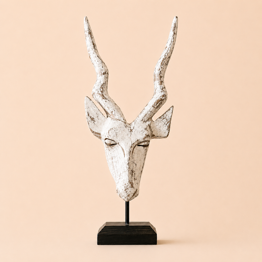 A wood carved antelope head on a stand with a white washed antique colouration on a beige background.