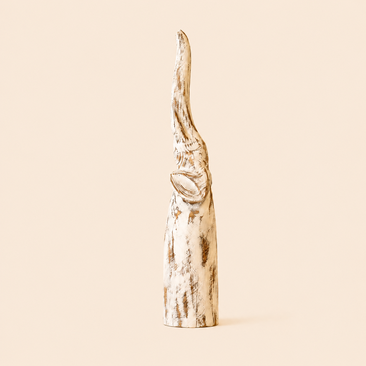 Antique white-washed Elephant carving with trunk up on a beige background.