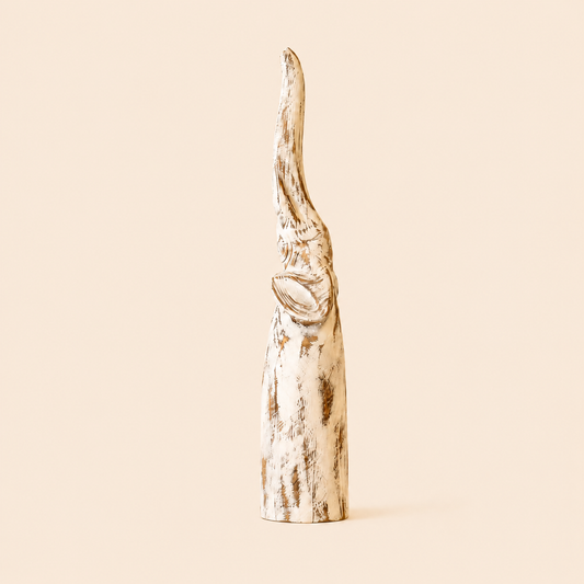 Antique white-washed Elephant carving with trunk up on a beige background.